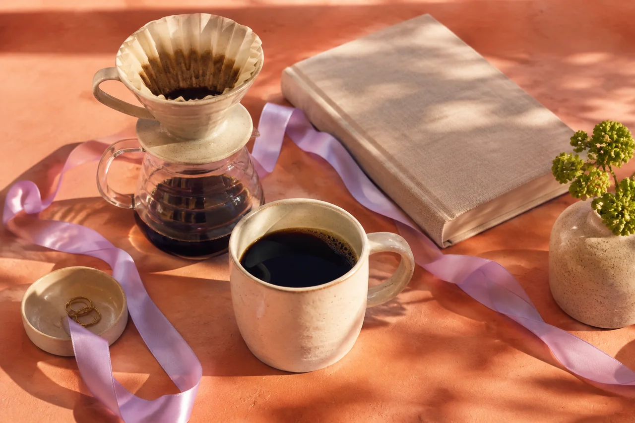 Keramikkopp, kaffe og en bok i varmt morgenlys.